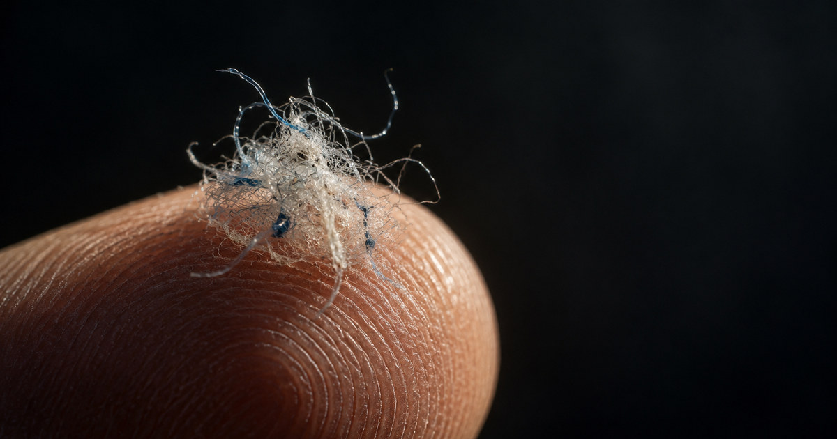 Imagen ilustrativa generada; no documenta el caso. Macro de una maraña de microfibras sintéticas recogidas del filtro de una lavadora, sobre la yema de un dedo.
